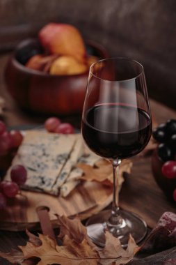 Koyu ahşap arka planda mavi peynirle servis edilen bir bardak kırmızı şarap. Sonbahar pikniği şarap ve peynir tabağı, meyve ve kuru yapraklar kırsal tarzda