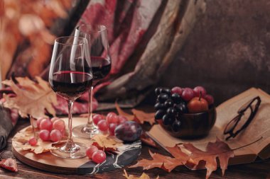 Sonbahar, iki kadeh kırmızı şarap, üzüm, kitap ve kuru yaprakla dolu, kır tarzı, koyu ahşap arka planda. Romantik kazak havası, fotokopi alanlı şarap tatma konsepti