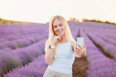 Lavanta tarlası. Sarı saçlı güzel bir kadın cep telefonlu lavanta çiçeklerinin arasında yürüyor, selfie çekiyor, sosyal ağlarda iletişim kuruyor, dinleniyor, dinleniyor, doğanın tadını çıkarıyor.