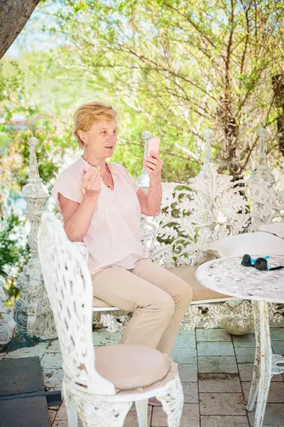 Mature attractive woman traveler sitting alone on the terrace of coffee shop in beautiful park in Bulgaria and using mobile phone. Active life of the elderly in retirement, active seniors