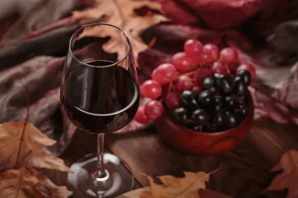 濃い木の背景にフルーツを添えた豊かな赤ワインのグラス 秋はまだ素朴なスタイルでワイン ブドウ 乾燥した葉で生きています セーター気象コンセプト — ストック写真