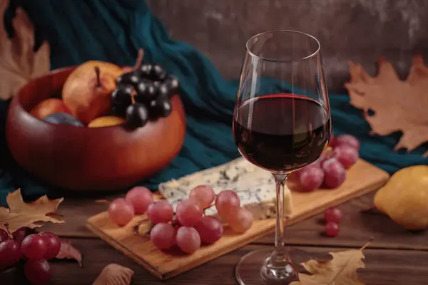 赤ワインのグラスは 濃い木の背景に青いチーズを添えました ロマンチックなスタイルのワインとチーズのプラッター 果物と乾燥した葉と秋のピクニック — ストック写真