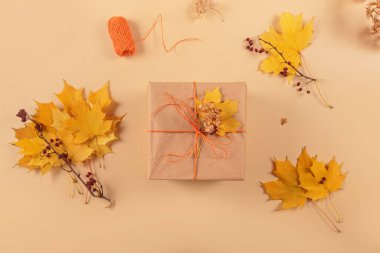 Sonbahar yaratıcı tatil hediyesi. El yapımı kağıt hediye kutusu ve bej masa üzerinde yapraklar. Hediye paketi. Şükran Günü, sonbahar tatili, sonbahar geçmişi