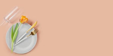 Çatal bıçak takımı ve pembe arka planda turuncu laleleri olan boş tabak. Bayram yemeği veya etkinlik için zarif bir düzenek..