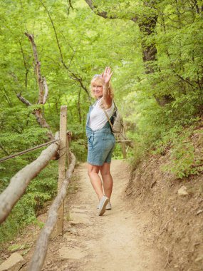 Orta yaşlı şort giymiş bir kadın sırt çantasıyla orman yolunda yürüyor. Çekici kadın gezgin yürüyüş parkurunda rahatlıyor ve doğanın tadını çıkarıyor. Zihinsel detoks ve fiziksel sağlık kavramı