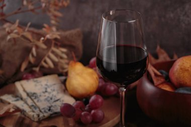 Koyu ahşap arka planda mavi peynirle servis edilen bir bardak kırmızı şarap. Sonbahar pikniği şarap ve peynir tabağı, meyve ve kuru yapraklar kırsal tarzda