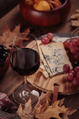 Koyu ahşap arka planda mavi peynirle servis edilen bir bardak kırmızı şarap. Sonbahar pikniği şarap ve peynir tabağı, meyve ve kuru yapraklar kırsal tarzda