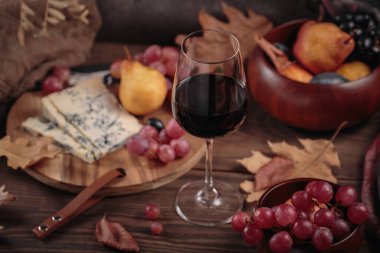 Koyu ahşap arka planda mavi peynirle servis edilen bir bardak kırmızı şarap. Sonbahar pikniği şarap ve peynir tabağı, meyve ve kuru yapraklar kırsal tarzda