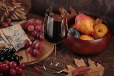 Koyu ahşap arka planda mavi peynirle servis edilen bir bardak kırmızı şarap. Sonbahar pikniği şarap ve peynir tabağı, meyve ve kuru yapraklar kırsal tarzda