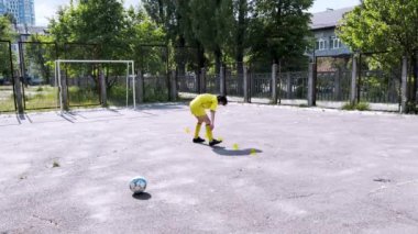Sarı elbiseli genç bir çocuk tek başına futbol oynuyor. Oyun sahasında, yeteneklerini geliştiriyor ve oyundan zevk alıyor. Yüksek kaliteli FullHD görüntüler