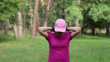 Pembe spor giyimli mutlu bir kadın parkta çalışıyor, formda ve aktif bir yaşam tarzını destekliyor. Yüksek kaliteli FullHD görüntüler