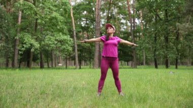 Pembe spor kıyafetleri içinde mutlu bir kadın parkta egzersiz yapıyor, pozitif ve sağlıklı bir yaşam tarzını somutlaştırıyor. Yüksek kaliteli FullHD görüntüler