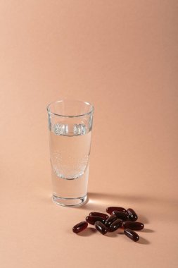 Diyet, beslenme, sağlıklı yeme konsepti. Bej arka plana kahverengi softgels kapsülleri dökmek için gıda takviyeleri ve bir bardak su dolu yağlı kapsüller..