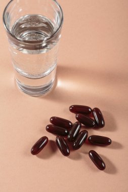 Diyet, beslenme, sağlıklı yeme konsepti. Bej arka plana kahverengi softgels kapsülleri dökmek için gıda takviyeleri ve bir bardak su dolu yağlı kapsüller..