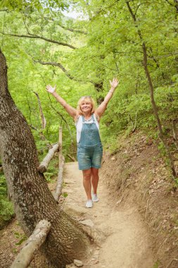 Orta yaşlı şort giymiş bir kadın sırt çantasıyla orman yolunda yürüyor. Çekici kadın gezgin yürüyüş parkurunda rahatlıyor ve doğanın tadını çıkarıyor. Seyahat ve sağlıklı yaşam tarzı
