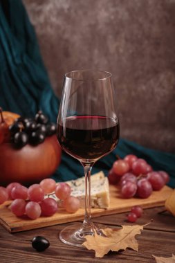 Koyu ahşap arka planda mavi peynirle servis edilen bir bardak kırmızı şarap. Sonbahar pikniği şarap ve peynir tabağı, meyve ve kuru yapraklar kırsal tarzda