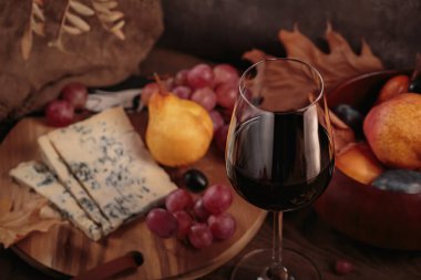 Koyu ahşap arka planda mavi peynirle servis edilen bir bardak kırmızı şarap. Sonbahar pikniği şarap ve peynir tabağı, meyve ve kuru yapraklar kırsal tarzda