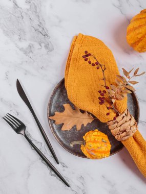 Arka planda balkabağı süslemeleri olan sonbahar masası ayarı. Siyah tabak, çatal bıçak takımı, sarı keten peçete ve kuru yapraklar. Sonbahar tatili, Cadılar Bayramı, Şükran Günü konsepti. Üst manzara, düz uzanma