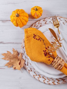 Beyaz ahşap arka planda balkabağı süslemeleri olan sonbahar masası. Boş tabak, çatal bıçak takımı, sarı keten peçete ve kuru yapraklar. Sonbahar tatili, Cadılar Bayramı, Şükran Günü konsepti. Üst görünüm