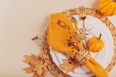 Arka planda balkabağı süslemeleri olan sonbahar masası ayarı. Boş tabak, çatal bıçak takımı, sarı keten peçete ve kuru yapraklar. Sonbahar tatili, Cadılar Bayramı, Şükran Günü konsepti. Üst manzara, düz uzanma