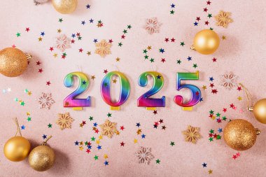 Işıl ışıl bir geçmiş tatili. Mutlu yıllar 2025. Gökkuşağı renkli mumlar, arka planda festival dekoru ve yıldızları 2025 yılı rakamlarıyla. Yeni yıl tebrik kartı. Üst manzara, düz uzanma