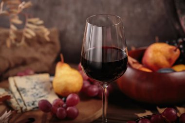 Koyu ahşap arka planda mavi peynirle servis edilen bir bardak kırmızı şarap. Sonbahar pikniği şarap ve peynir tabağı, meyve ve kuru yapraklar kırsal tarzda