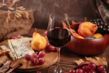 Koyu ahşap arka planda mavi peynirle servis edilen bir bardak kırmızı şarap. Sonbahar pikniği şarap ve peynir tabağı, meyve ve kuru yapraklar kırsal tarzda
