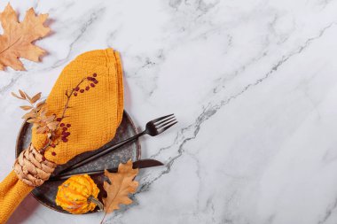 Arka planda balkabağı süslemeleri olan sonbahar masası ayarı. Siyah tabak, çatal bıçak takımı, sarı keten peçete ve kuru yapraklar. Sonbahar tatili, Cadılar Bayramı, Şükran Günü konsepti. Üst manzara, düz uzanma