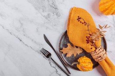 Arka planda balkabağı süslemeleri olan sonbahar masası ayarı. Siyah tabak, çatal bıçak takımı, sarı keten peçete ve kuru yapraklar. Sonbahar tatili, Cadılar Bayramı, Şükran Günü konsepti. Üst manzara, düz uzanma