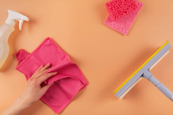 Набор для мытья окон и других поверхностей на оранжевом фоне. Женская рука с тряпкой. Концепция уборки, профессиональная уборка, бытовые принадлежности. Вид сверху, плоский с копировальным пространством