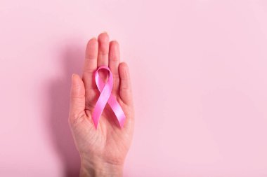 Bir kadında bulunan pembe kurdele göğüs kanseri farkındalığını temsil eden açık pembe bir arkaplan verir. Yumuşak tonlarda bakım ve destek, sağlık kampanyaları için ideal..