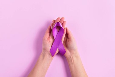Pembe arka planda iki kadın eli tarafından tutulan mor kurdele pankreas kanseri desteği ve dayanışmasını simgeliyor. Sağlık hizmetleri girişimleri ve savunma kampanyaları için ideal.