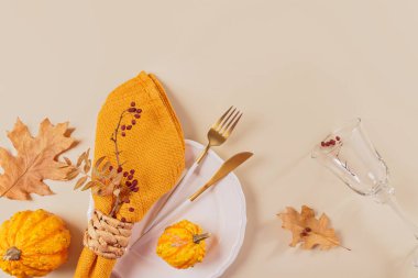 Arka planda balkabağı süslemeleri olan sonbahar masası ayarı. Boş tabak, bardak, çatal bıçak takımı, sarı peçete ve kuru yapraklar. Sonbahar tatili, Cadılar Bayramı, Şükran Günü konsepti. Üst manzara, düz uzanma
