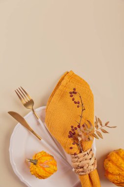 Arka planda balkabağı süslemeleri olan sonbahar masası ayarı. Boş tabak, çatal bıçak takımı, sarı keten peçete ve kuru yapraklar. Sonbahar tatili, Cadılar Bayramı, Şükran Günü konsepti. Üst manzara, düz uzanma