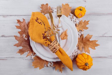 Beyaz ahşap arka planda balkabağı süslemeleri olan sonbahar masası. Boş tabak, sarı keten peçete ve kuru sonbahar yaprakları. Sonbahar tatili, Cadılar Bayramı, Şükran Günü konsepti. Düz yatıyordu