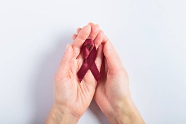 İki kadının elindeki bordo kurdele beyaz bir arkaplan veriyor. Çoklu miyelom hastalığından etkilenenlere bakımı ve desteği simgeliyor. Sağlık kampanyaları ve para toplama kampanyaları için ideal..