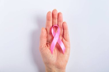 Beyaz arka planda pembe bir kurdele tutan bir kadın, göğüs kanseri hastalarına destek ve dayanışmayı simgeliyor. Farkındalık projeleri ve sağlık mesajları için mükemmel.