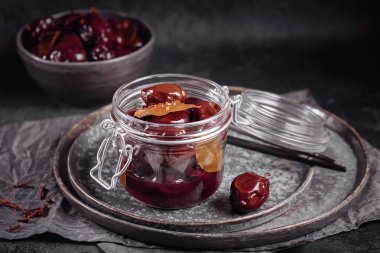 Marinated plums with spices in glass jar on the kitchen table. Homemade canning. Vegetable snack for winter.
