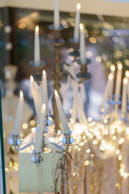 Dekoratif gümüş bir şamdanın yakın plan görüntüsü. Parlayan ışıklarla çevrili birkaç beyaz mum ve karmaşık bir iç mekan ortamında bulanık bokeh..