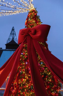 Parlayan peri ışıkları, canlı kırmızı kurdeleler ve büyük kırmızı kadife bir fiyonkla süslenmiş çarpıcı bir Noel ağacı lüks ve şenlikli bir akşam atmosferi yaratıyor..