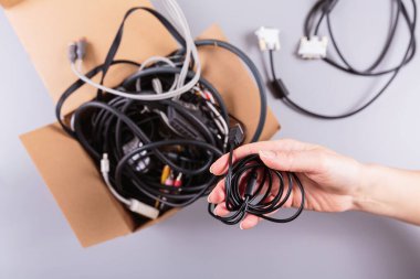 Kadınların elleri, elektronik atıkların geri dönüşümünün önemini vurgulayan eski elektronik aksesuarları karton konteynırın yanında tutuyorlar.