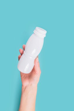 Rahatlatıcı mavi bir arka planda, bir kadının eli beyaz bir plastik şişe tutarak gezegenin korunmasında bireysel eylemlerin önemini vurgular..