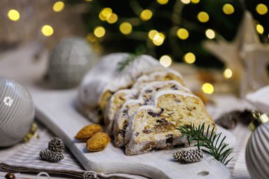 Badem, kozalak, yemyeşil dallar ve şenlikli ve rahat bir kış ortamında ışıl ışıl parlayan Noel ışıklarıyla süslenmiş taşralı ahşap bir tahtanın üzerinde dilimlenmiş klasik bir pasta..