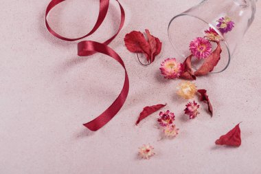 Kurdele ve kırmızı kurumuş çiçeklerle dolu cam kadehten sonbahar kompozisyonu ve bej arka planda yapraklar. Sonbahar arkaplanı