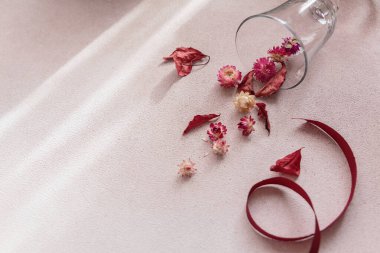 Kurdele ve kırmızı kurumuş çiçek ve bej arkaplanda yapraklarla dolu şarap kadehinden sonbahar kompozisyonu. Güneş ışığı ve gölgeli sonbahar arkaplanı