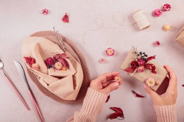 Kurumuş çiçeklerle süsleme işlemi. Oval tabaklar, çatal bıçak takımı, cam, hediye kutusu ve doğal süslemeler. Bayram bayramı için bayram masası servis eden bir kadın, Şükran Günü. Üst görünüm