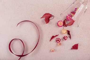 Kurdele ve kırmızı kurumuş çiçeklerle dolu cam kadehten sonbahar kompozisyonu ve bej arka planda yapraklar. Sonbahar arkaplanı