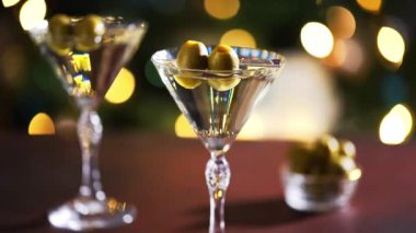 Kristal bardakta klasik bir martini, yeşil zeytinler altın çevre ışıklarını yansıtıyor..