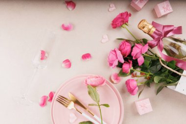 Pembe tabaklar, altın çatal bıçak takımı, şampanya flütü ve taze çiçeklerin yer aldığı romantik bir ortam için rahat ve zarif bir masa..