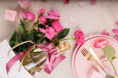 Pembe tabaklar, altın çatal bıçak, şampanya bardağı, taze güller ve kalp süslemelerinin yer aldığı yumuşak ve romantik bir akşam yemeği..